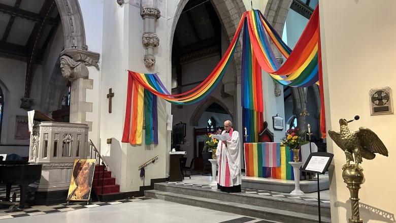 A church officials speaks on an alter decorated with Pride flags and decorations. 