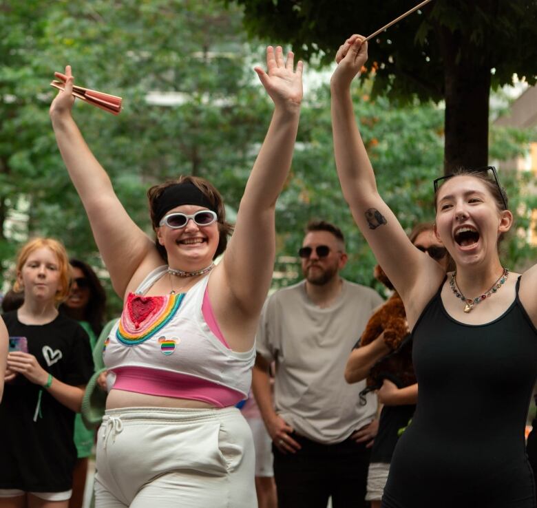 A person is pictured wearing rainbow flags with their hands up cheering. 