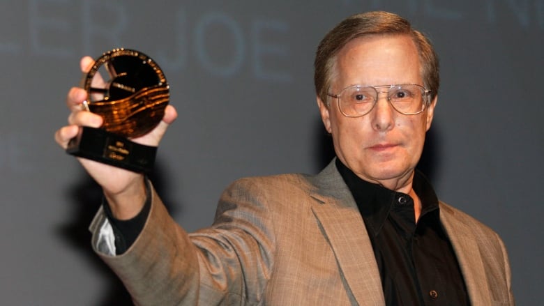 A bespectacled man holds up a small trophy.