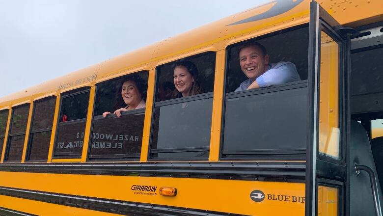 Two women and a man stand inside a school bus with their faces visible through open windows. 