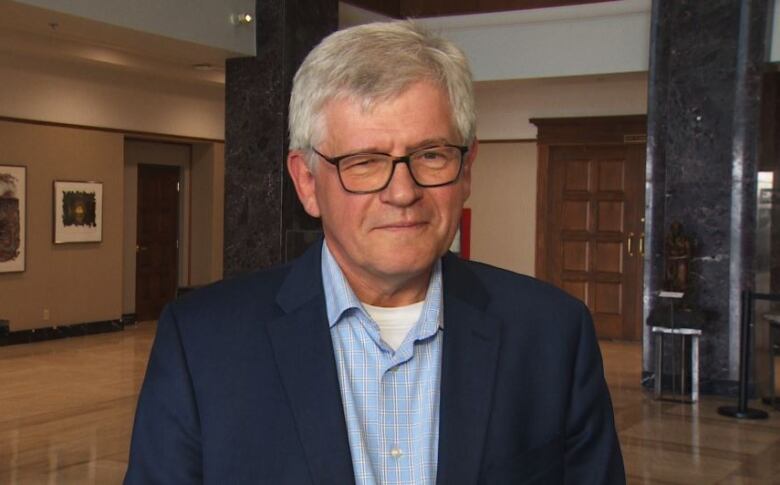 A man with grey hair and glasses standing in a lobby. 