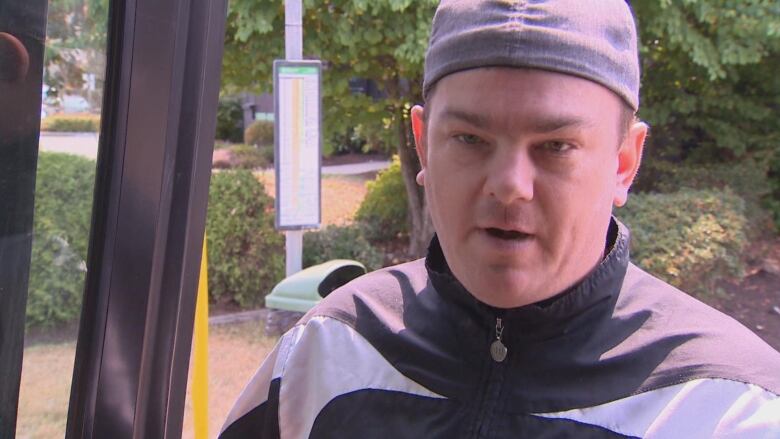 A man in the door of a bus speaks to the camera.