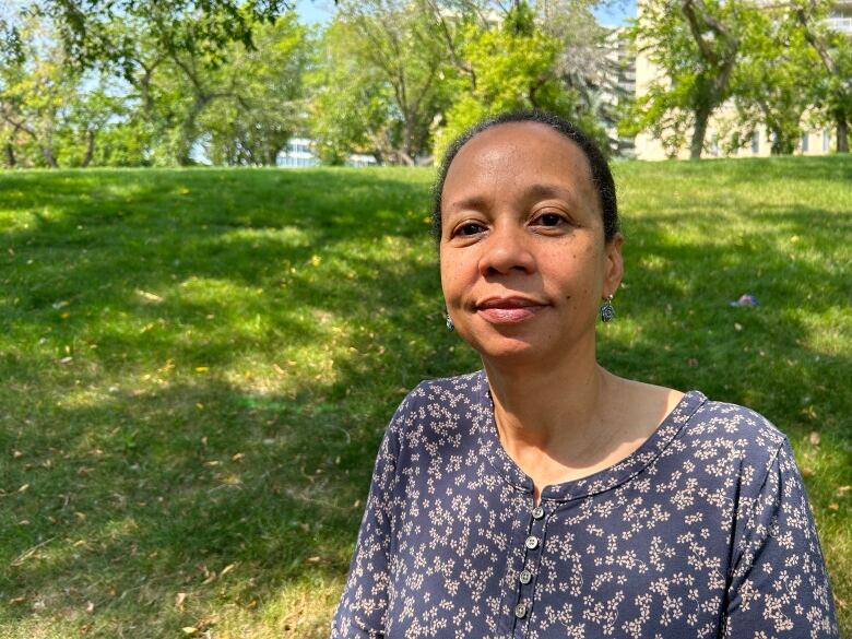 A woman in a blue top with floral prints stands in a park.