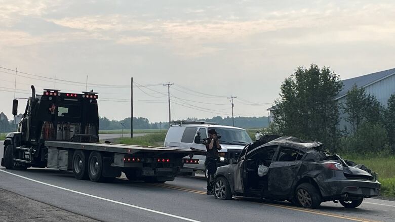 A smashed car on the side of the road near a tow truck. 