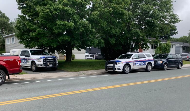 Police vehicles are parked in the driveway and on the street outside a home on a residential street.