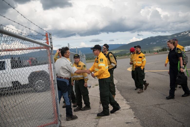 A group of firefighters in yellow shirts are seen being greeted on an airport tarmac.