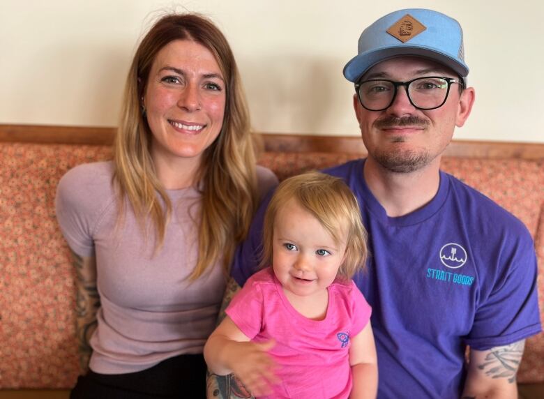 Smiling young couple pose with a child aged about two in a pink shirt. 