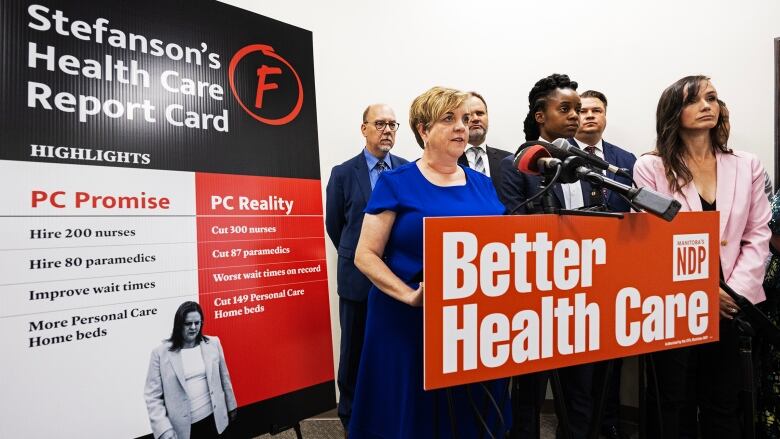 Several people stand at a podium, while a poster for 'Stefanson's Health Care Report Card' is shown. 