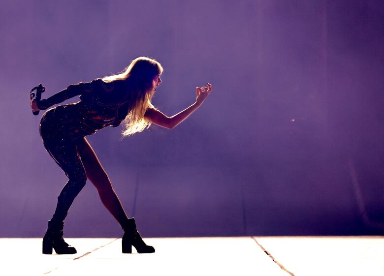 Taylor Swift backlit on stage and gesturing to someone not pictured, while performing.