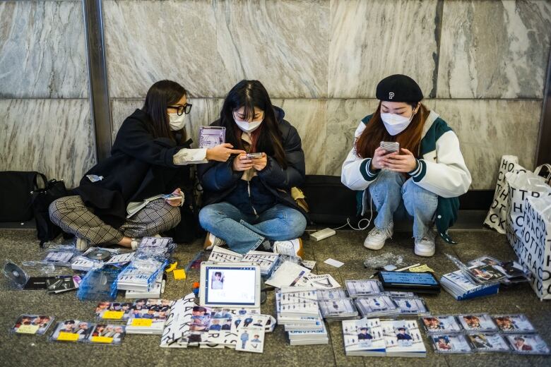 Three Asian women look through piles of cards with photos of boy band members.