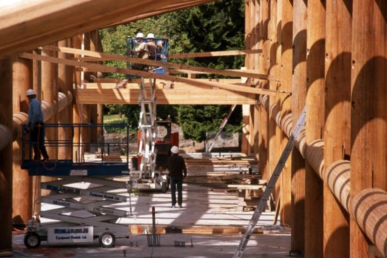 Four construction workers are in the middle of a construction zone of a large wooden frame of a building. 