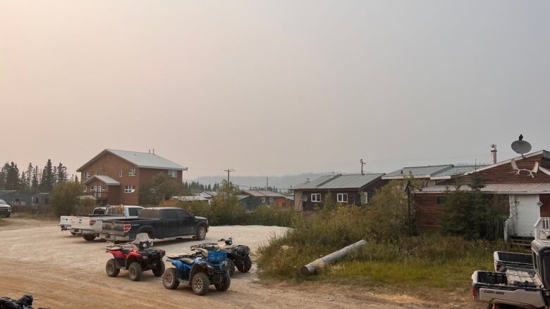 A smoky haze blankets Old Crow, Yukon, on Wednesday. Houses, trucks and ATVs are seen with the river in the background. Residents report that at times, the smoke has been so thick that they can't see across the river.