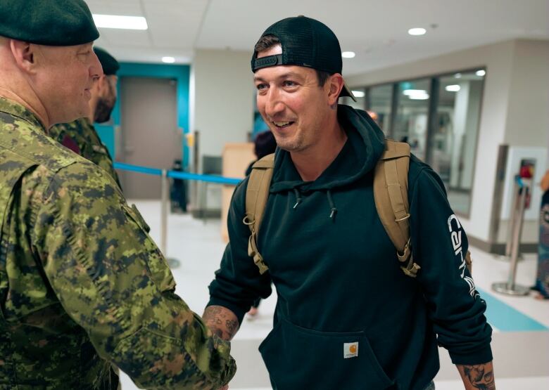 A man is greeted by a soldier in uniform at an airport. 