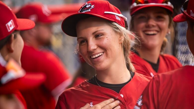 A woman in a baseball uniform laughs while talking to her teammates. 