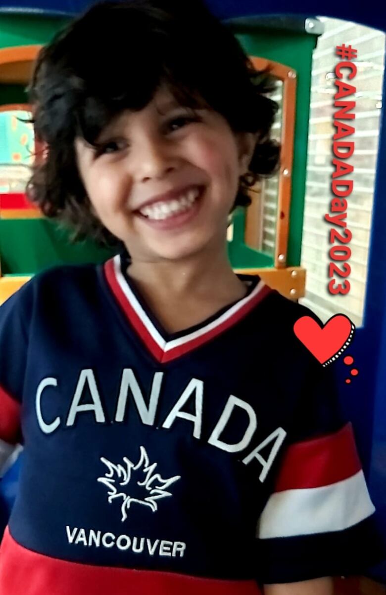 A toddler wearing a blue shirt that says Canada smiles in this close up.