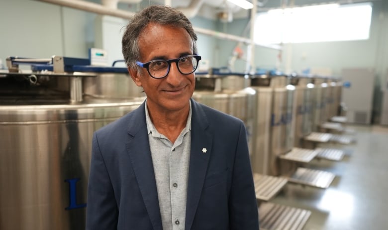 A man with greyish hair wears glasses and a blue blazer.