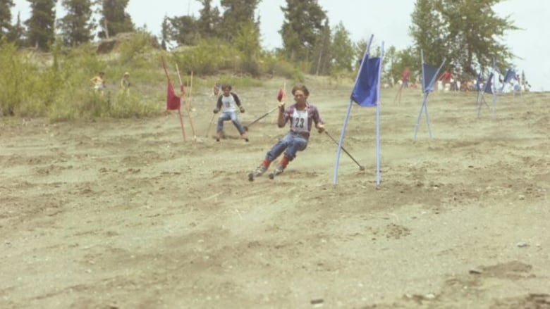 Two people on downhill skis race down a steep, sandy slope.