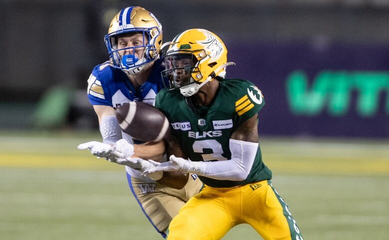 Two football players reach for the football at the same time.