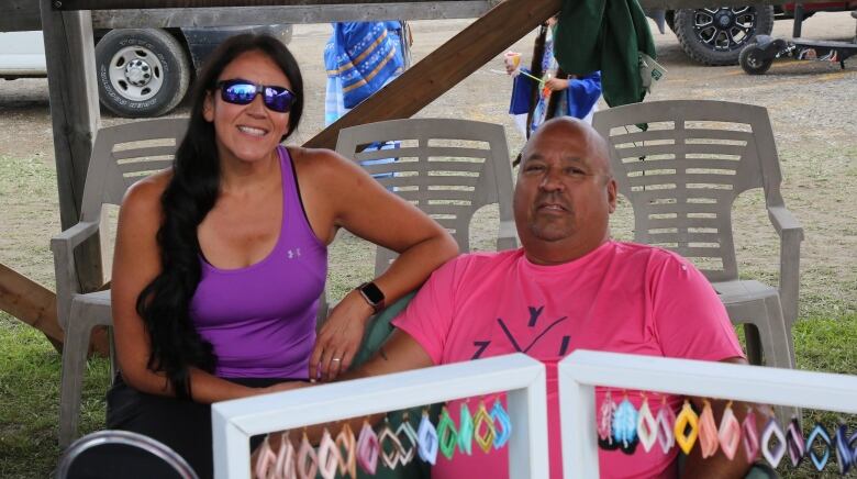 A woman and man sit on chairs. Earrings are displayed in front of them.