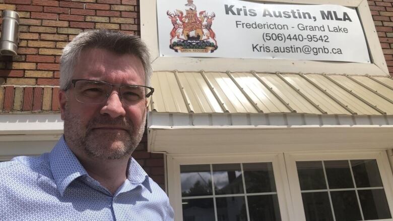 Kris Austin poses for a photo under his MLA office sign