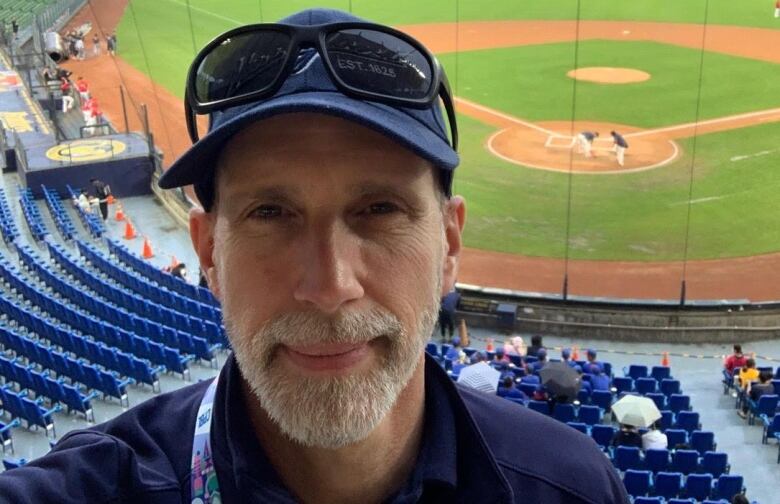 A selfie of a man standing in the stands at a baseball game with the diamond seen behind him.