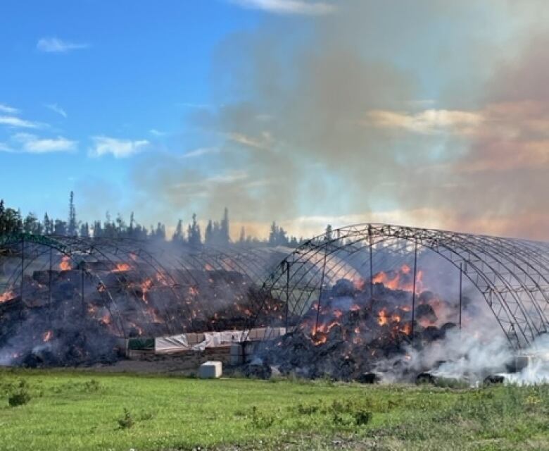 Embers smoulder in the burned-out skeleton of a hay barn that was recently on fire.