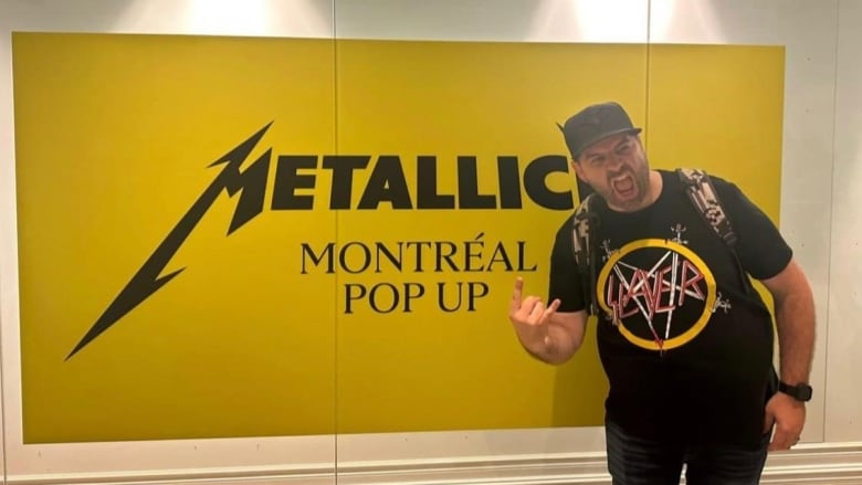 A man makes a rockstar hand gesture in front of a Metallica pop up sign.