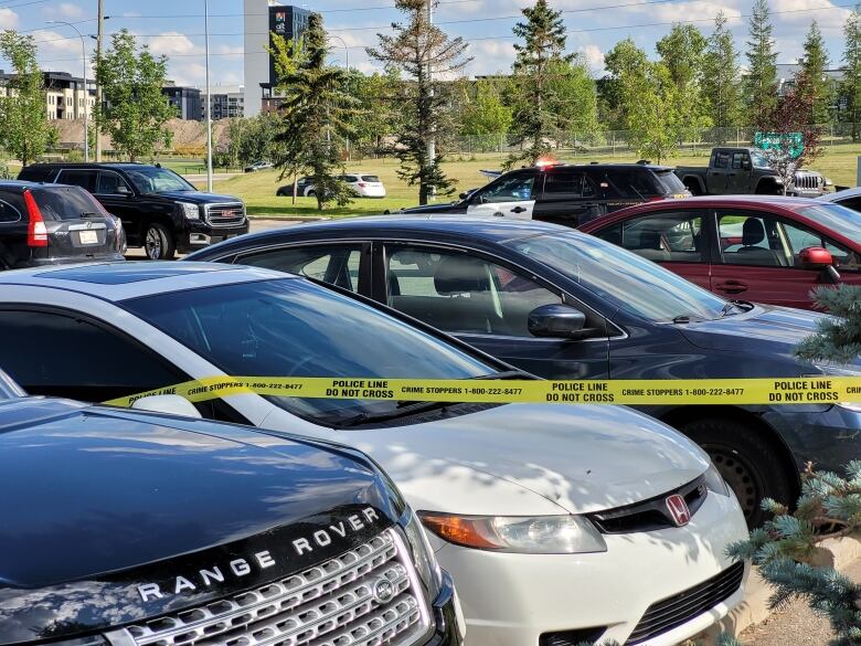 Cars are surrounded by yellow police tape at a parking lot.