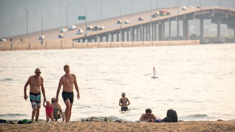 Grandfather walks with his son and grandchild on a beach in Kelowna, B.C.,