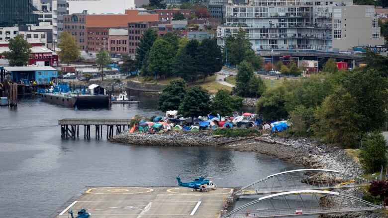 Wide view of helicopters parked in a helipad, and colorful tents at CRAB Park with Downtown Vancouver in the background. 