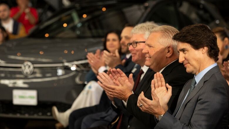 Men sit in a line clapping hands. 