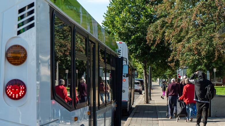 People walk along a sidewalk next to a bus on a sunny day.