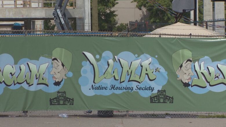 A poster is attached to a fence with a cartoony image of a man in goatee and logo advertising Lu'ma Native Housing Society. 