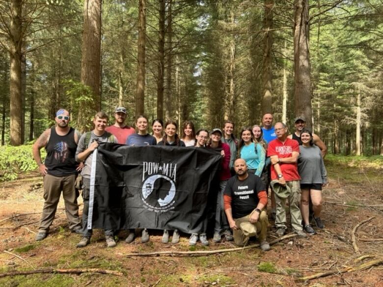 A group of people pose together in a wooded area, holding a large black flag.