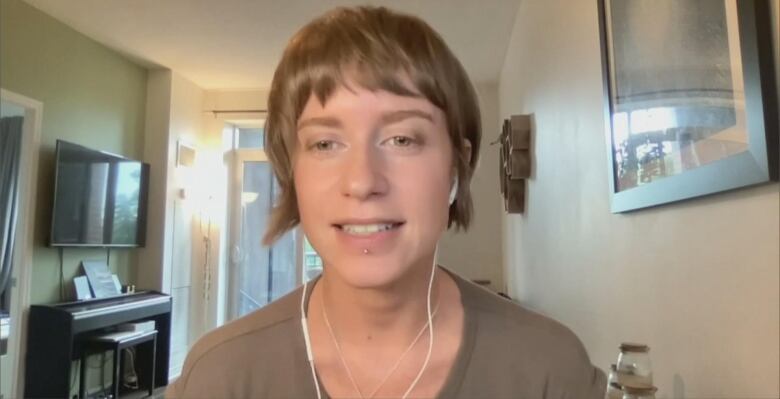 A woman with short hair in a brown tshirt sits in front of the camera wearing headphones. 