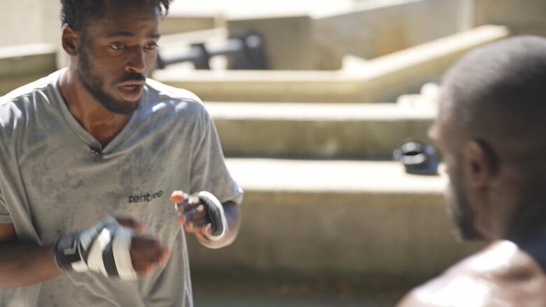 A man spars in a training session with wraps around his two hands and sweat on his T-shirt.