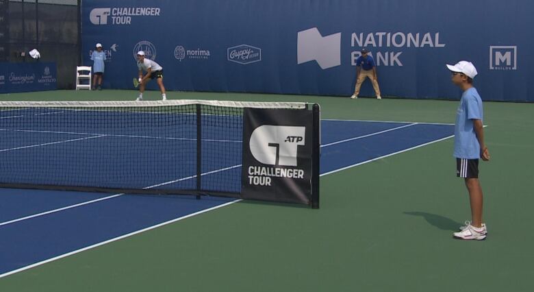 A kid in a blue shirt stands at the net 