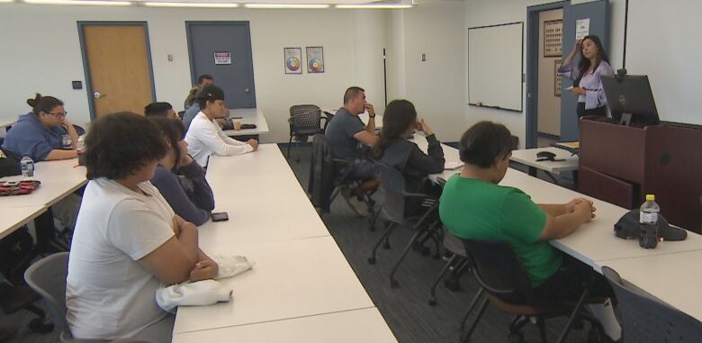 A classroom setting with a woman lecturer in front and youth listening to her.