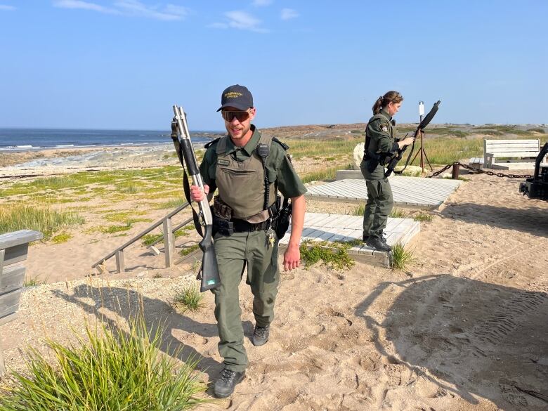 Two conservation officers with shotguns near a beach.