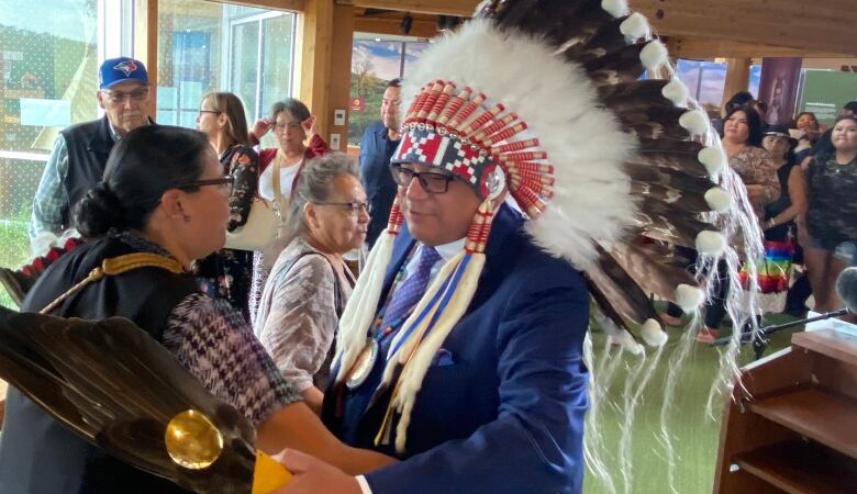 A man in a feathered headdress is surrounded by people in a room.