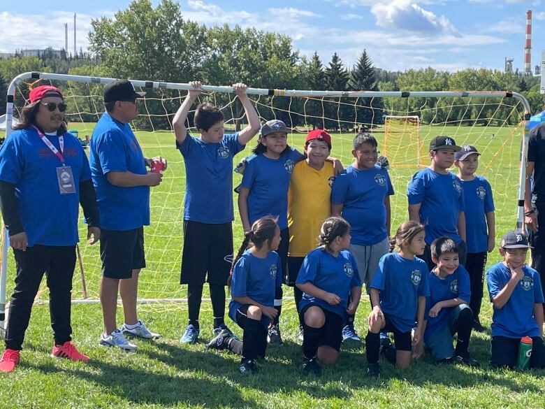 Boys and girls in blue shirts stand in front of a soccer net.