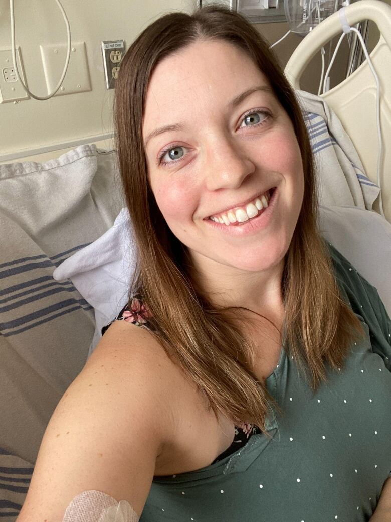 A woman smiles and takes a selfie in a hospital room. 