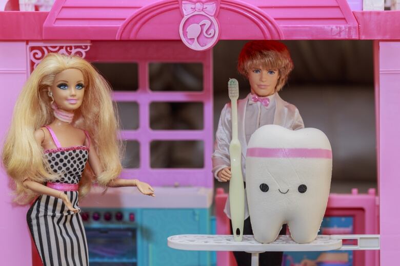 A Barbie doll with big, blond hair next to Ken doll with a large tooth and toothbrush.