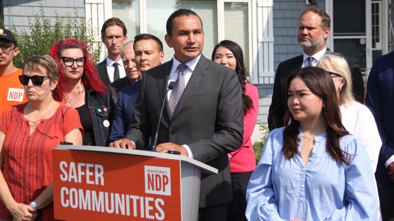 A man speaks at a podium, while several people surround them.