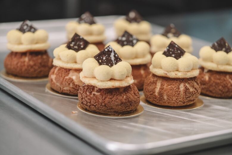 Several round, golden pastries sit on a baking tray. They have a cracked surface and are each topped with a square of chocolate.