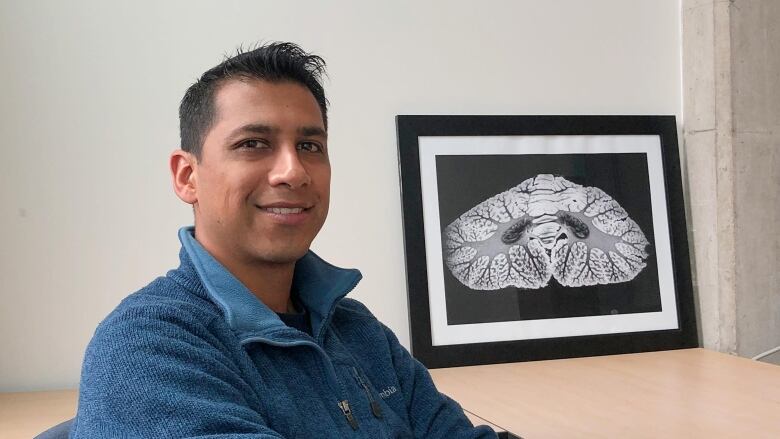 A man seated at an office desk smiles at the camera. 