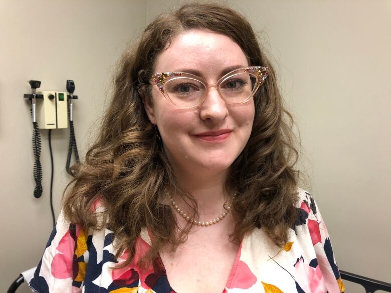 Woman with shoulder-length brown curly hair wearing glasses and flowery blouse.