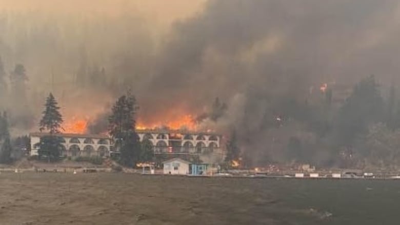 Flames and smoke can be seen rising from a white hotel building from across a stretch of water.