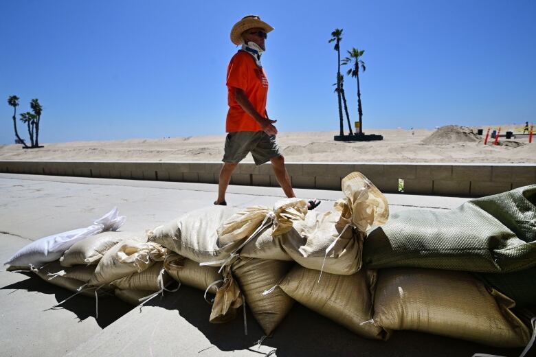 Man walking past sandbags piled near beach-front homes in Seal Beach, Calif., ahead of the presumed arrival of Hurricane Hilary.