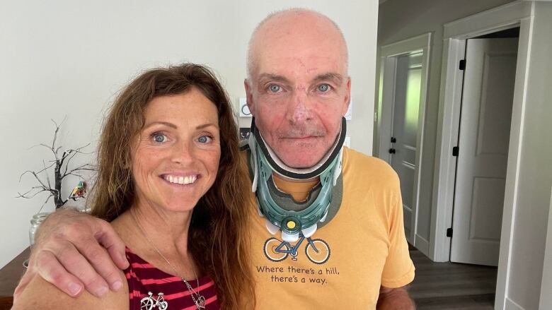 A selfie of a smiling woman and a man, with his arm around her, wearing a neck brace.